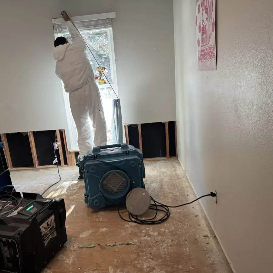Technician in a protective suit working above flood-cut walls while a dehumidifier runs in a Golden hallway