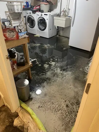 Laundry room floor covered in water from a washer leak, with a hose ready for extraction