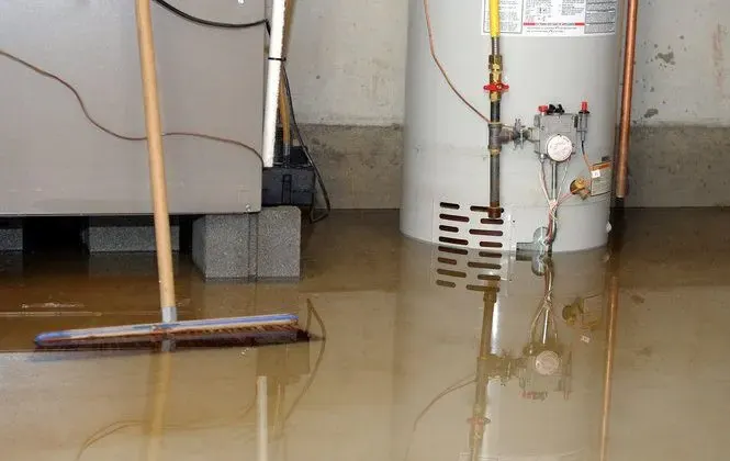 Basement floor flooded around a gas water heater with a push broom in the water